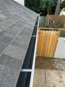 top view of grey shingled roof with cleaned gutter above wooden fence